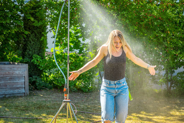Junge Frau beim Abkühlen unter dem Rasensprenger im Garten der Dr. Loew Einrichtung Jugendbetreuung