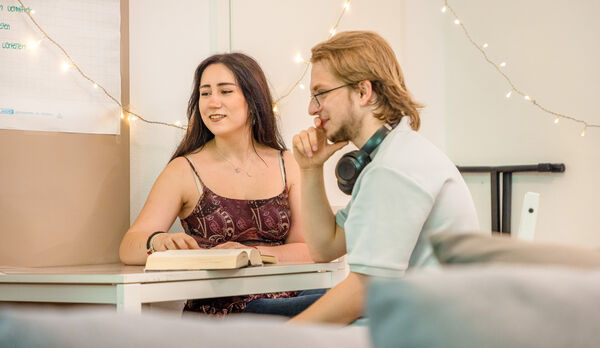 Zwei junge Menschen im Gespräch an einem Tisch mit Buch in der Dr. Loew Einrichtung Jugendbetreuung