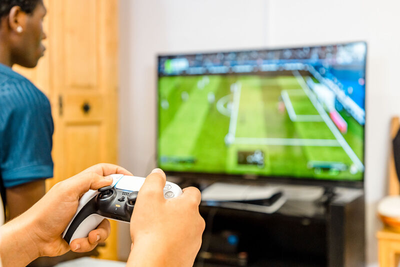 Jugendlicher spielt mit einem Controller ein Fußball-Videospiel im Gemeinschaftsraum