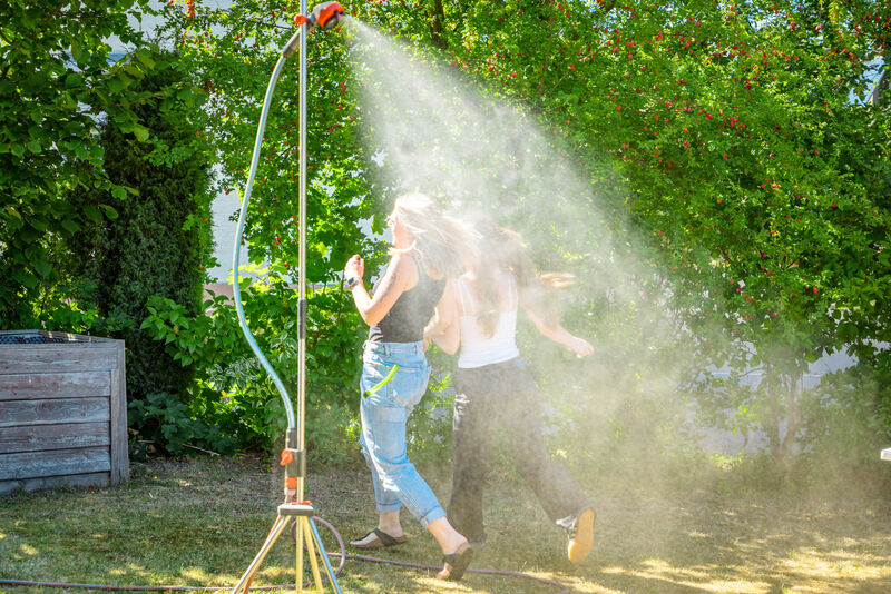 Mitarbeiterin kühlt sich aus Spaß unter einer Gartendusche im Garten der Wohngruppe ab