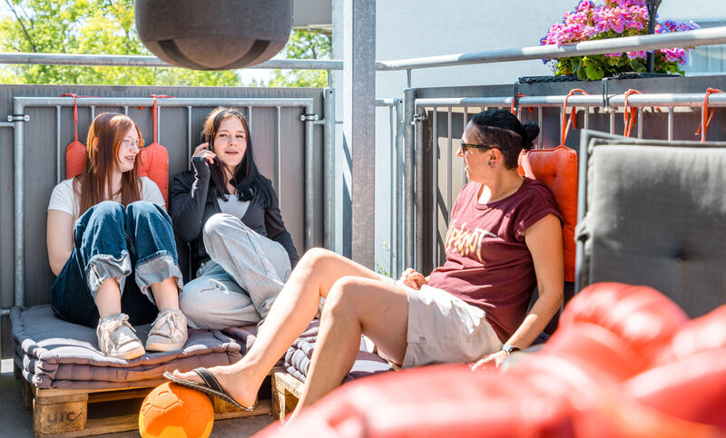 Zwei Jugendliche und eine Mitarbeiterin sitzen gemeinsam auf der Terrasse der Jugendwohngruppe Isabelle