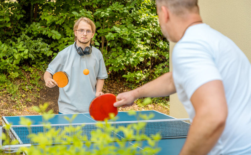 Jugendlicher und Mitarbeiter spielen gemeinsam Tischtennis im Garten