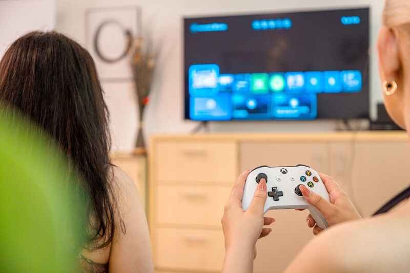 Jugendliche spielen gemeinsam mit einem Controller ein Videospiel im Wohnbereich