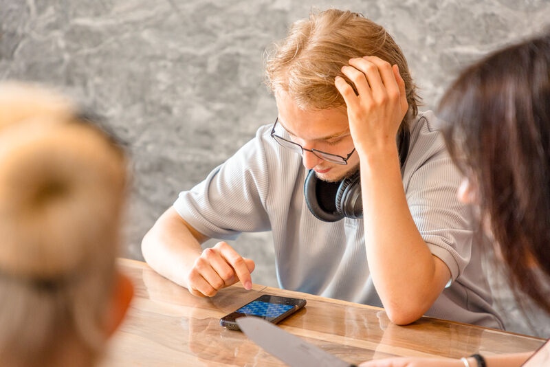ugendlicher sitzt mit Kopfhörern am Tisch und nutzt ein Smartphone ugendlicher sitzt mit Kopfhörern am Tisch und nutzt ein Smartphone