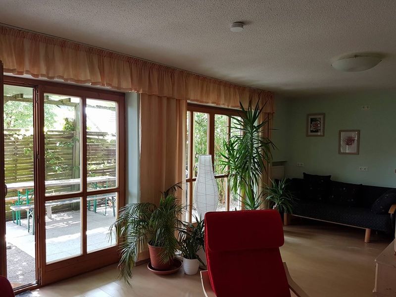 Haus Schwalbenweg – heller Wohnraum mit Gartenblick Wohnbereich im Haus Schwalbenweg der Dr. Loew Einrichtungen mit großen Fenstern und Pflanzen